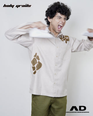 Angry man tearing paper, wearing a beige full sleeve shirt with brown abstract patterns and green shorts.
