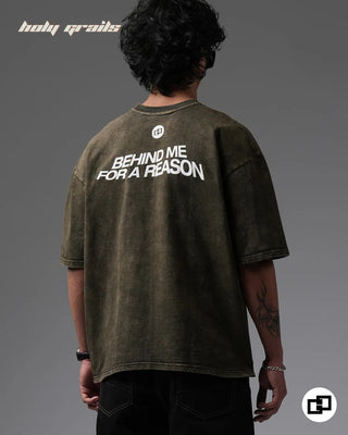 Person wearing a 'Behind For A Reason' Olive Green 240 GSM 100% Cotton Oversized Acid Wash T-Shirt with text on the back against a gray background - Back