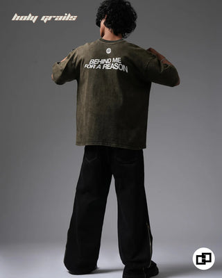 Person wearing a 'Behind For A Reason' Olive Green 240 GSM 100% Cotton Oversized Acid Wash T-Shirt with text on the back, standing against a gray background - Back Full