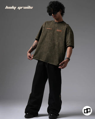 Person wearing a 'Behind For A Reason' Olive Green 240 GSM 100% Cotton Oversized Acid Wash T-Shirt and black pants on a gray background - Front Full