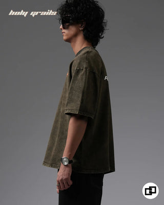 Person wearing a 'Behind For A Reason' Olive Green 240 GSM 100% Cotton Oversized Acid Wash T-Shirt with a brand logo on a gray background - Side 2