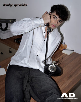 Men lying on a wooden table with a vintage phone, wearing a street style 'Cuff Script' White Pintex Cotton Pleated Designer Shirt - Front