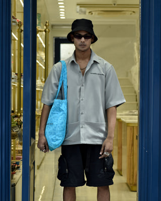 Standing Men Wearing Streetwear 'Kangaroo Grey Oversized Shirt' with black shorts and a cap hanging a blue bag on the right shoulder - Front