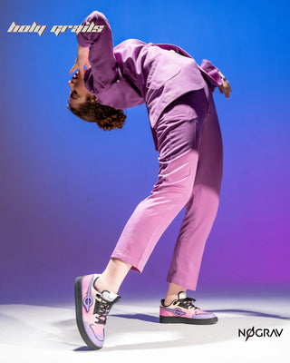 A model in a purple tracksuit and pink-and-purple sneakers poses dynamically against a blue-to-purple gradient studio background.